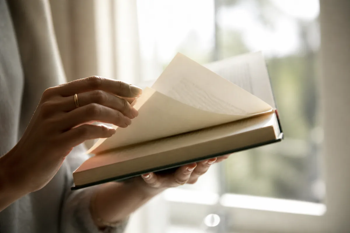 Une main feuilletant la table des matières d&rsquo;un livre relié près d&rsquo;une fenêtre